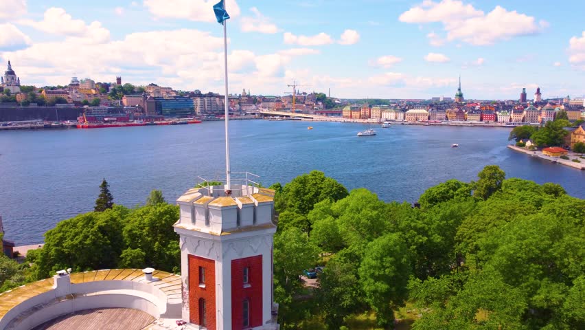 Aerial view capturing Kastellet in Stockholm with a Swedish flag waving, surrounded by lush greenery and overlooking the scenic waterfront and cityscape.