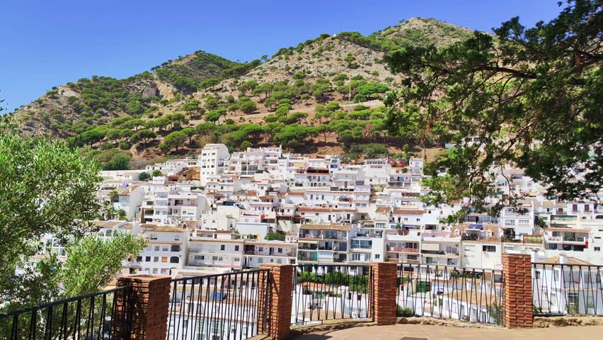 Panoramic static view of typical andalusian white village Mijas located on the Costa del Sol, Spain. A lot of white washed houses, mountains and pine forest in the background. Sunny weather, blue sky.