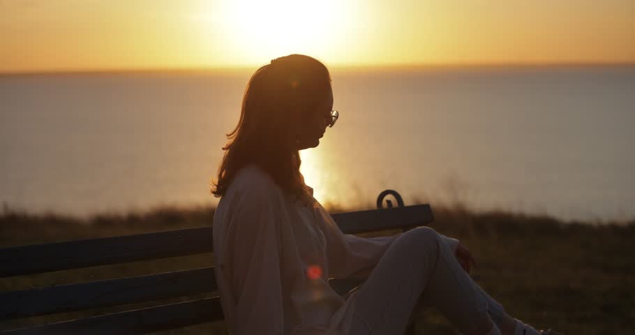 Silhouette of woman sitting and resting looking at sea sunset, slow motion