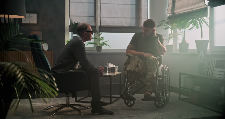Senior psychologist supports military man with disability. Male soldier in wheelchair shakes hands with psychotherapist after therapy session or rehabilitation. Psychological help and mental health.