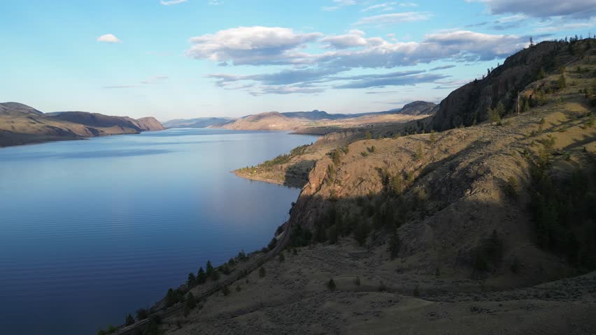 Aerial view of a large deep blue lake with mountains and a valley in the background on a nice sunny day with white fluffy clouds in the sky. British Columbia, Canada.