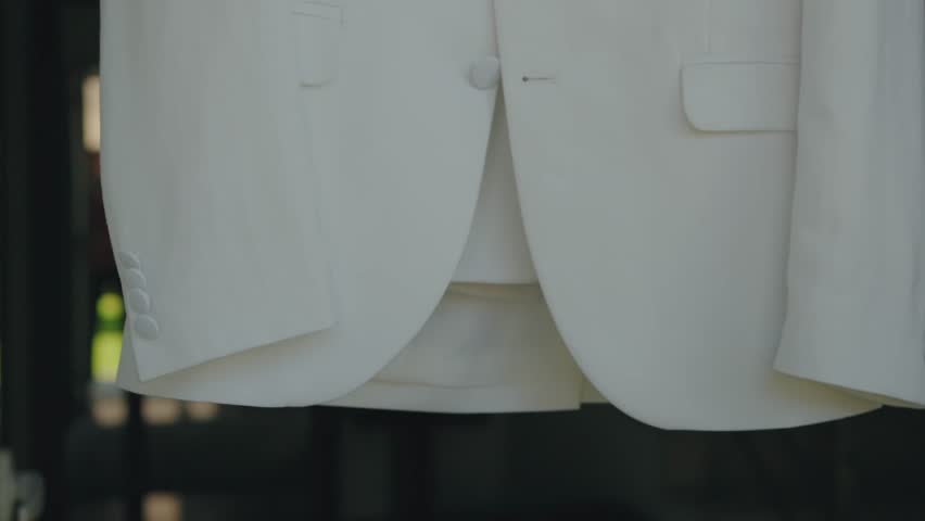 detailed close-up of a white suit jacket hanging, ready for the groom to wear for the wedding ceremony
