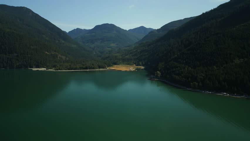 Aerial shot around the lakes edge of Harrison Lake in British Columbia Canada on a hazy sunny morning with the large emerald lake water sitting very still and calm surrounded by hills of green trees