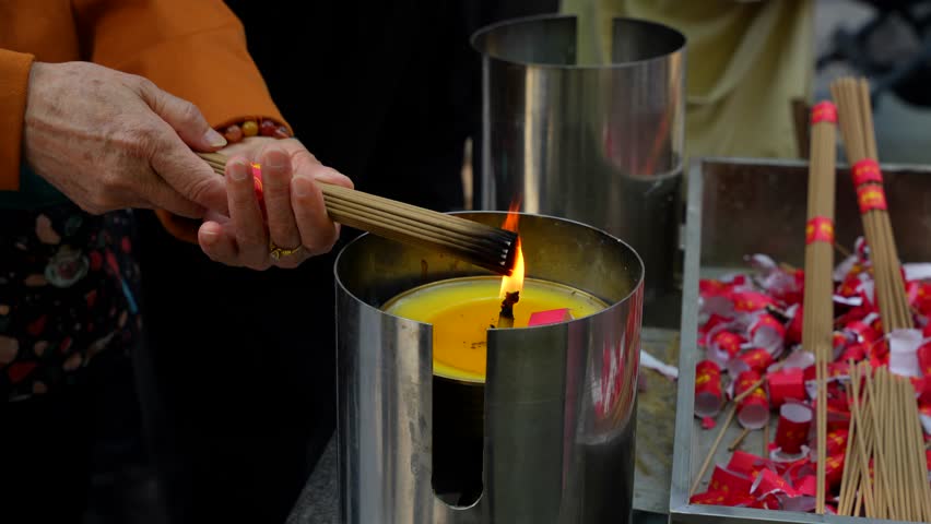 Close-up of old female hands lighting incense sticks for prayer and reflection in a Chinese temple