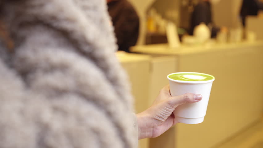 4K Happy Asian woman drinking hot green tea latte during travel fish market in Tokyo city, Japan. People enjoy outdoor lifestyle eating street food and shopping at street market on holiday vacation.