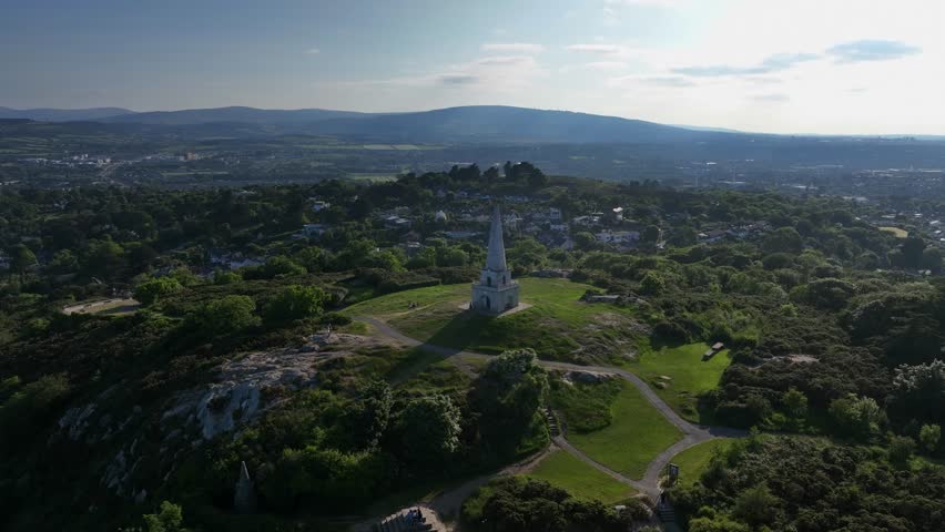 Killiney Hill, County Dublin, Ireland, June 2023. Drone slowly orbits The Obelisk clockwise gradually revealing the view north west towards Dún Laoghaire and Dublin City Center on a bright sunny day.
