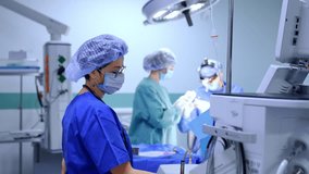 Female anesthesiologist stands looking at the apparatus in surgery room. Surgeon and scrub nurse work at operation at backdrop. - Powered by Shutterstock - Get 15% off with code: PIKWIZARD15