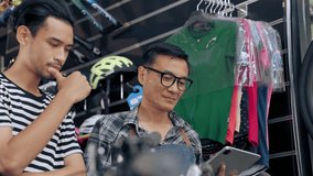 Asian young man purchaser conversation with senior Asian salesman by using tablet checking price and specification bike shop store. Small business and dealer concept - Powered by Shutterstock - Get 15% off with code: PIKWIZARD15
