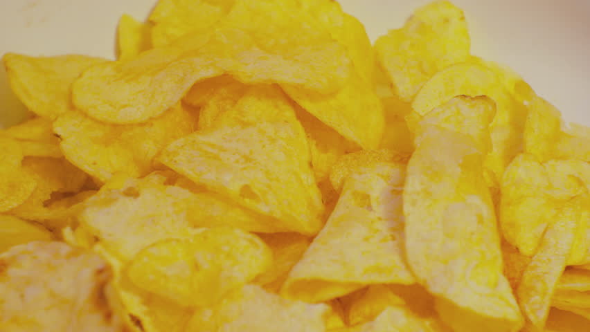 Modern food. Unhealthy eating. Hand takes a lot of potato chips from a bowl. Close-up. Slow motion.