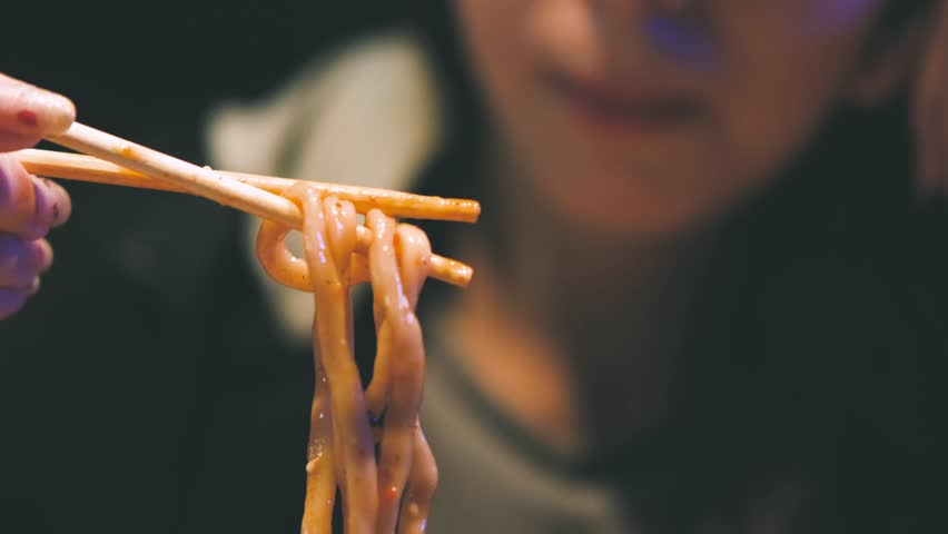 Teenage girl eating udon noodles with seafood in a pan-Asian restaurant.