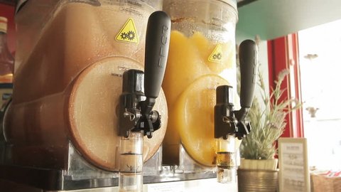 two moist juice machines contatining ice coffee and orange juice in a cafe