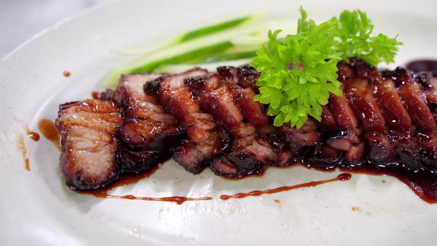 A close-up view of delicious char siu served on a plate alongside fresh cucumber slices.