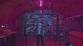 Young man solves equations in laboratory. Media. Student solves mathematical equations in secret classroom. Laboratory for experiments with mathematical calculations on blackboard - Powered by Shutterstock - Get 15% off with code: PIKWIZARD15