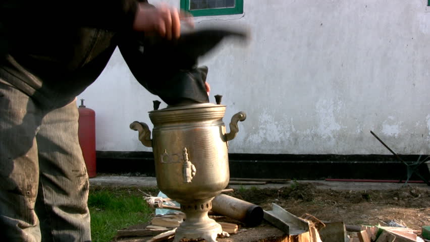 Man is blowing Russian samovar with wellingtons