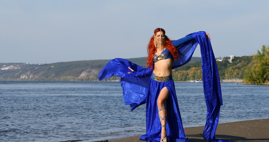 Redhead woman in blue dance costume posing on beach