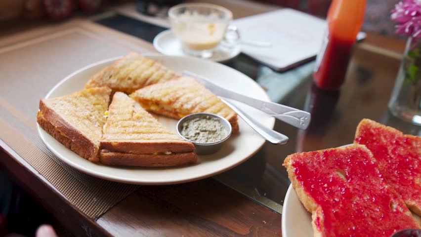 Closeup shot of a hand picking up sandwich from a plate while having breakfast in a café. Early morning breakfast background with copy space. Man eating breakfast at a restaurant outside.