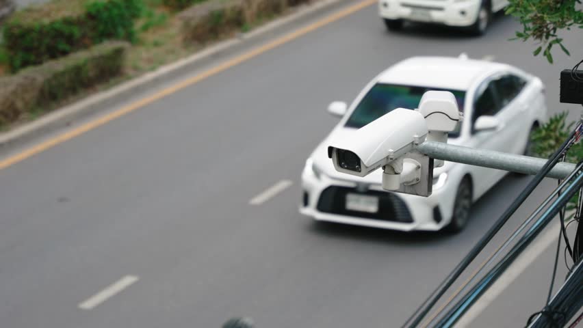 Close up of a surveillance enforcement camera monitor city traffic and speed control above the asphalt road. Defocused cars driving in the background. Road traffic safety copy space scene
