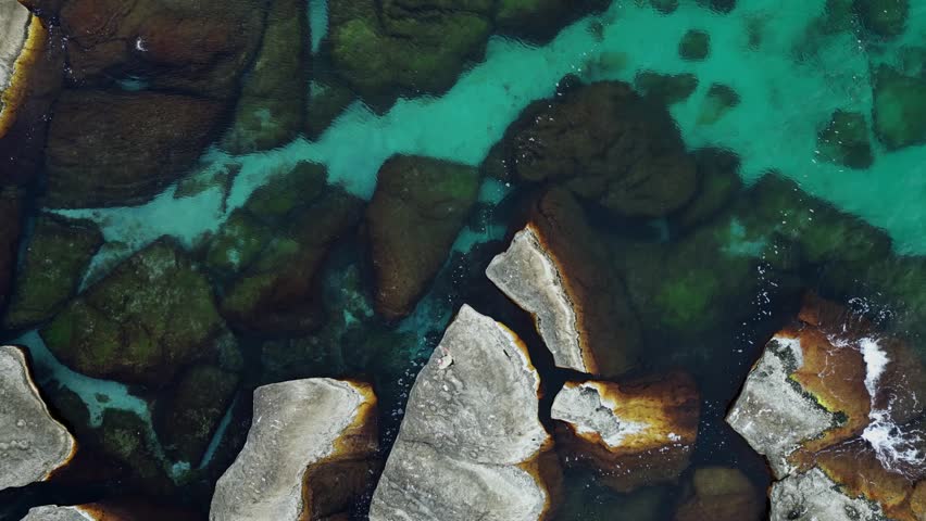 a young European man fishing with a spinning rod on a rocky seashore, top view from a drone, smooth departure
