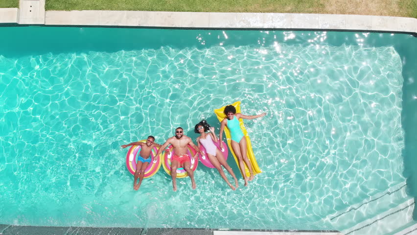 Aerial of african american parents, son and daughter lying on inflatables in sunny pool, copy space. Summer, family, fun, togetherness, vacations, free time, relaxation and lifestyle, unaltered.