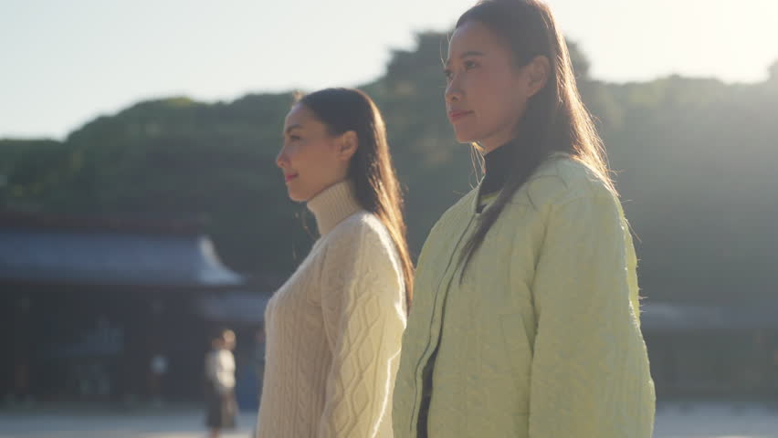 Two Asian woman friends praying in traditional Meiji Jingu Shrine in Tokyo city, Japan in autumn. People tourist travel Japan landmark famous place and learning Japanese culture on holiday vacation.