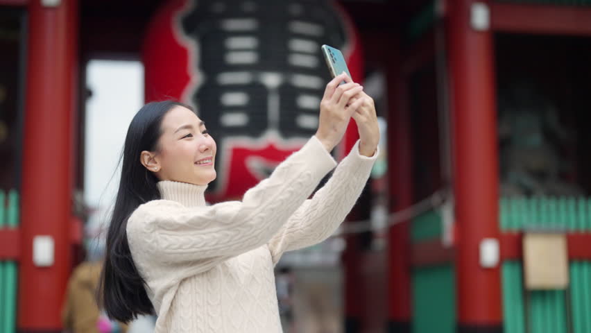 4K Happy Asian woman using mobile phone taking selfie during travel Sensoji Temple at Asakusa district, Tokyo, Japan. Attractive girl enjoy outdoor lifestyle travel city street on holiday vacation.