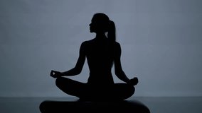 Silhouette, young woman meditates and does yoga in a dark room, the woman performs yoga elements while sitting on a stone near the water, calm mood. - Powered by Shutterstock - Get 15% off with code: PIKWIZARD15