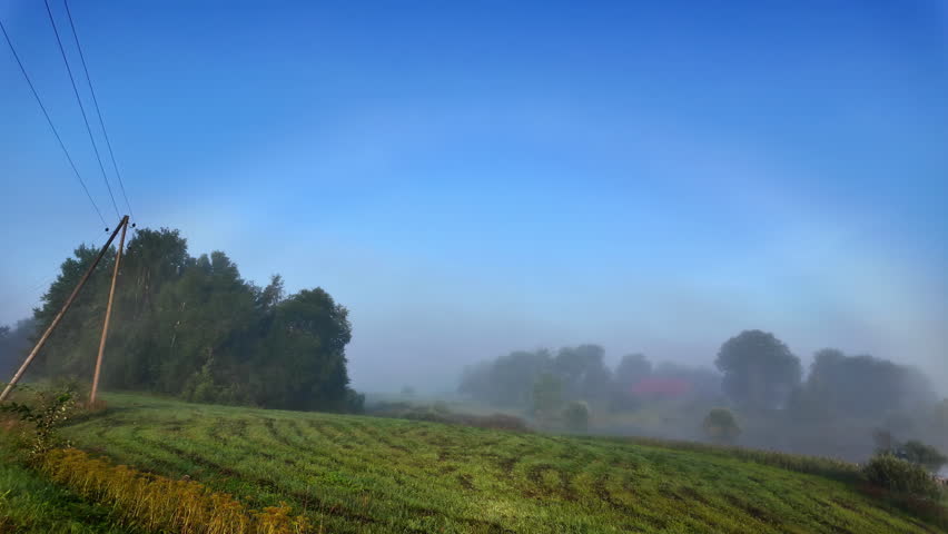 Foggy countryside field with soft morning light and a rainbow over misty trees and farmland