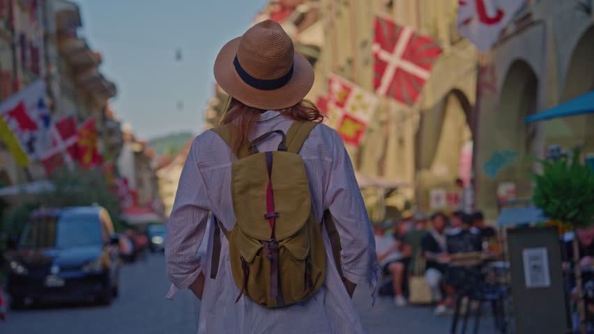 An attractive girl in a fashionable hat spends her holidays alone, traveling through the Alpine meadows. Tourist with a backpack travels through Switzerland with incredible views