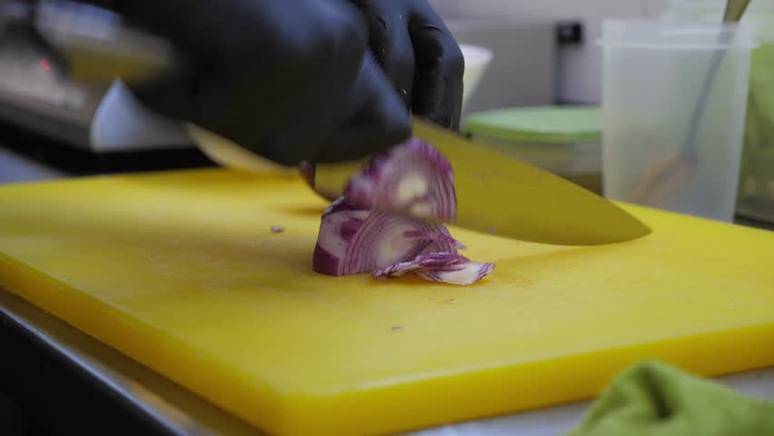 A close-up of a chef in gloves cutting red onions on a chopping board in a restaurant kitchen. 