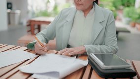 Close-up of Asian businesswoman writing notes and reviewing financial documents and writing notes outdoors, focusing on financial planning, accounting, and data analysis tasks. - Powered by Shutterstock - Get 15% off with code: PIKWIZARD15