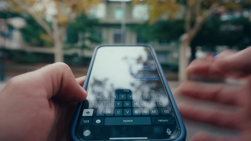 POV shot, close-up of a mans hands texting on a smartphone in a city street, the urban environment in the background.
