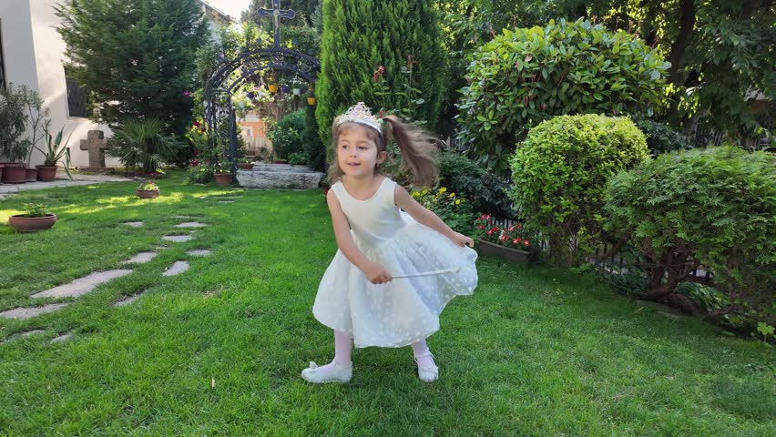 Little fairy girl in white dress and crown with magic wand dancing. Little girl dressed as fairy