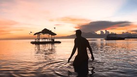 A man dives into a calm ocean and then swims away during a beautiful and colourful sunset on Paliton Beach in Suquijor Island, Philippines. The sky is full of shades of orange. - Powered by Shutterstock - Get 15% off with code: PIKWIZARD15