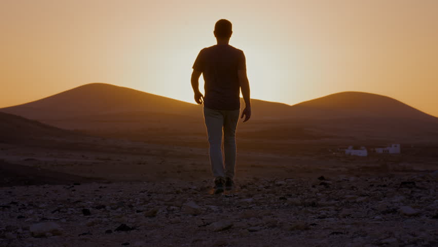 happy person raising arms and walking towards sunset at goldenhour with mountain range in the back