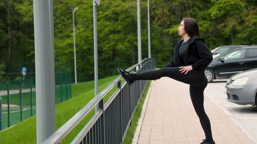 Young beautiful dark-haired athletic girl doing leg exercises outdoors in the park.slow motion
