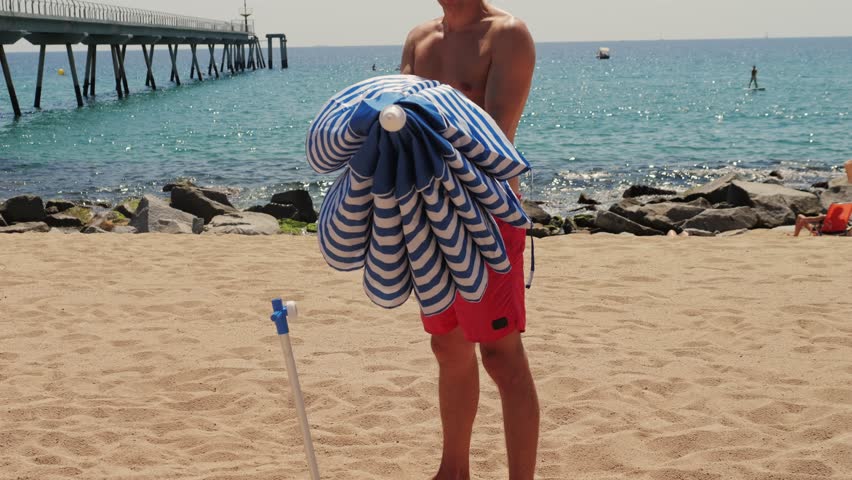 Man Tourist Enjoying a Relaxing Day at the Beach, Comfortably Seated Under a Bright Umbrella, Barcelona, spain.