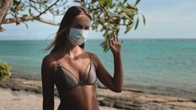 A stylish woman in a bikini soaks up the sun while responsibly donning a face mask, blending safety with seaside relaxation during the COVID-19 pandemic. - Powered by Shutterstock - Get 15% off with code: PIKWIZARD15