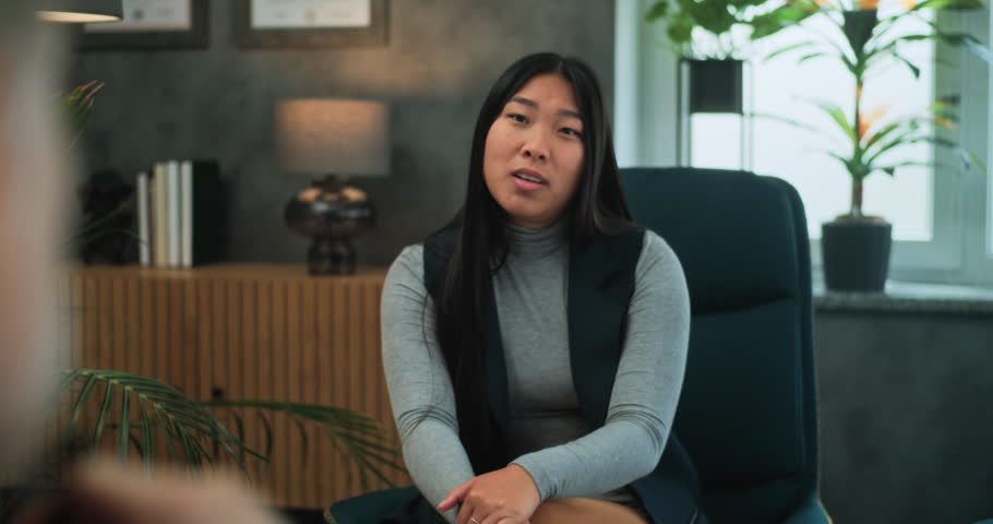 Asian young woman discusses relationship problems. Multiethnic couple on counseling session with psychologist. In the foreground, unfocused psychotherapist talks to young family during couples therapy