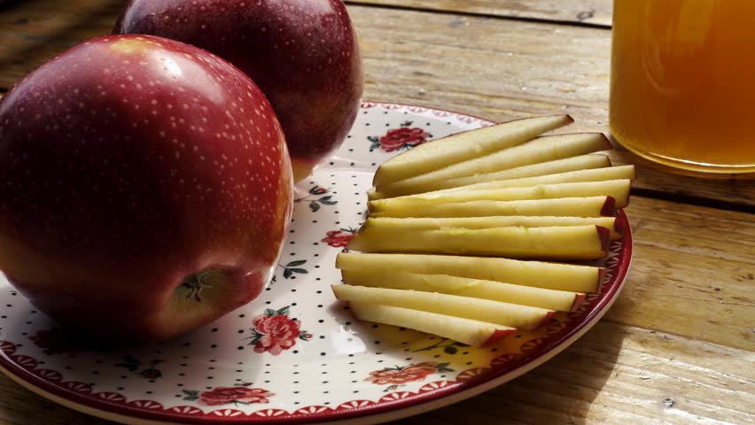 Apples red whole and sliced with a jar of honey on the traditional Jewish holiday of Rosh Hashana on a wooden table by the window on a sunny day. Close-up