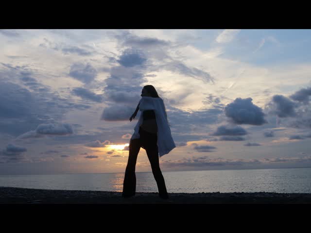 silhouette of one alone Young woman girl with flying hair dancing, jumping, having fun on sunset seaside. Happy female
 dance at sunrise on beach, coast. lady making hands movements. transparent dress