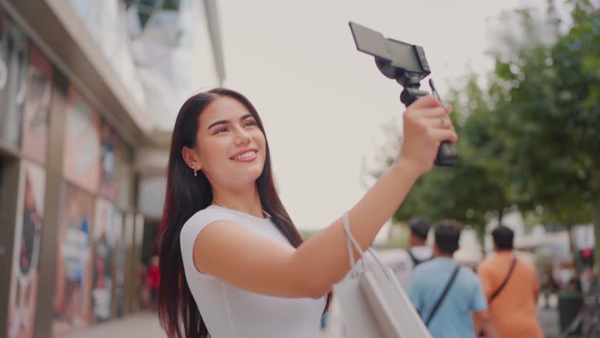 Mixed race woman traveler use camera record vlog while travel in city. Attractive female tourist feel happy and relax while walking on street, enjoy taking a photo during vacation trip in Frankfurt.
