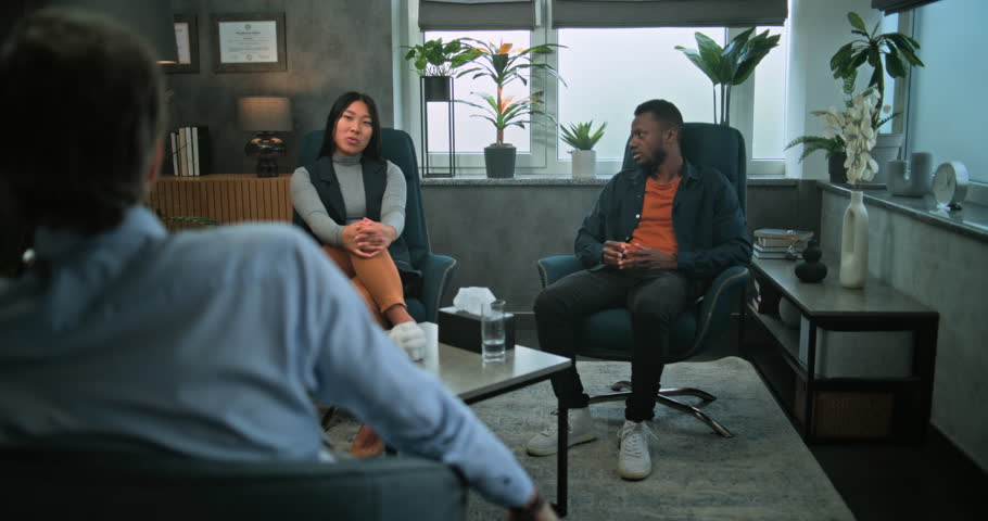 Back view of psychologist listening to multiethnic young couple on counseling session. African American boyfriend loses self control, shouts and starts fight with girlfriend during couples therapy.