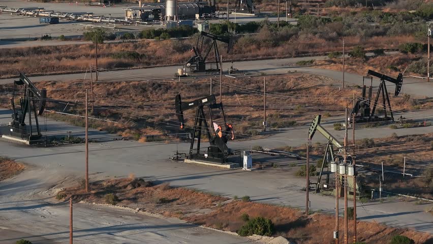 Aerial view of the oil rigs and wells in the Midway-Sunset shale oil fields, the largest in California. A pumpjack operates at an oil field. Oil pump rig energy industrial machine for petroleum.