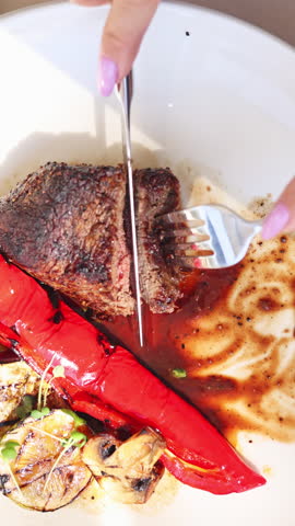 filet mignon,medium rare, on plate in restaurant and a glass of red wine on table. woman, girl, eating delicious dish. chef preparing on grill vegetables and meat.lady in office shirt. vertical video.