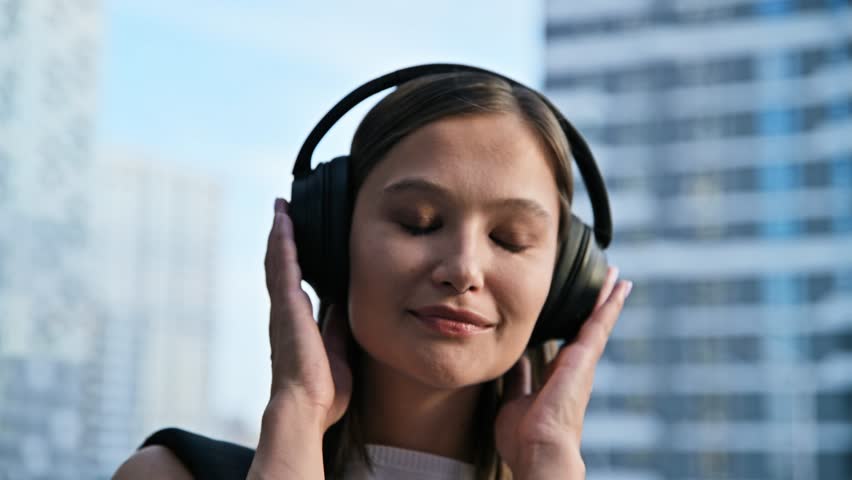 Happy beautiful young woman in headphones listening to music, outdoors