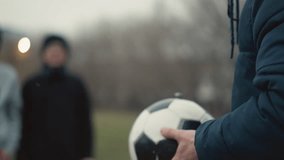 Close-up of a coach holding and turning a soccer ball in his hands, with a blurred view of two people standing in the background - Powered by Shutterstock - Get 15% off with code: PIKWIZARD15