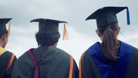 Three graduates are standing in front of a cloudy sky, wearing their caps and gowns. Scene is one of accomplishment and pride, as the graduates have just completed their studies - Powered by Shutterstock - Get 15% off with code: PIKWIZARD15