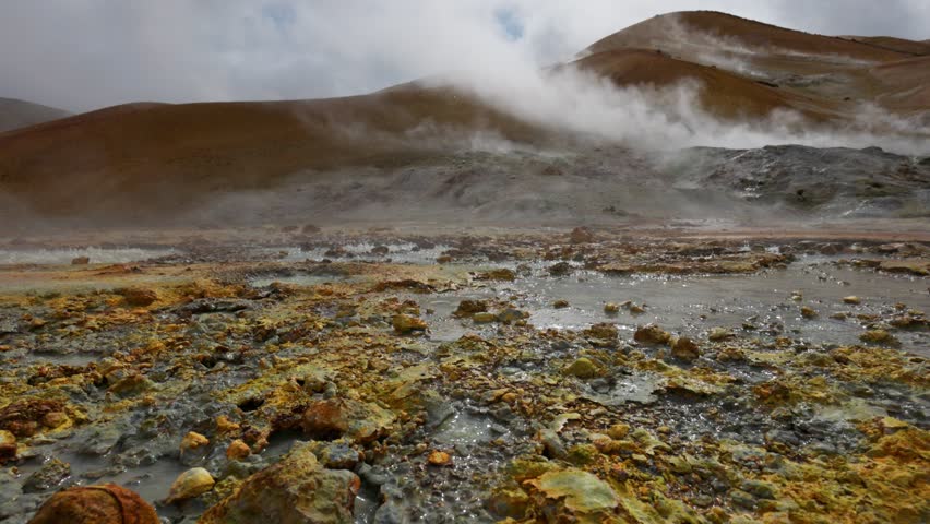 Geothermal area with hot springs gushing out from underground. Gimbal shot of red and grey soil with boiling water and steam. Geothermal energy