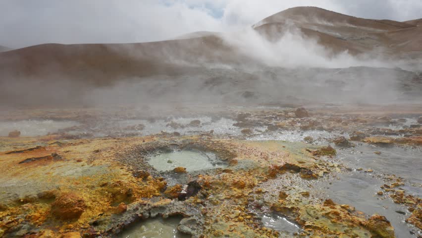 Geothermal area with hot springs gushing out from underground. Gimbal shot of red and grey soil with boiling water and steam. Geothermal energy