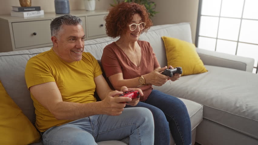 Joyful middle-aged couple playing video games together on a cozy living room couch at home